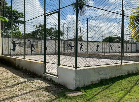 Quadra cercada com rede de vôlei e silhuetas de jogadores pintadas no muro