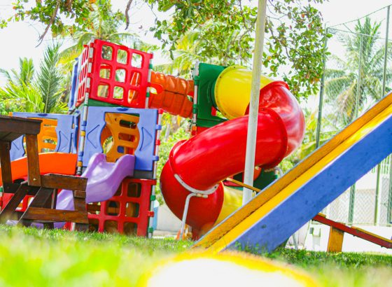 Playground infantil com tobogã vermelho e escorregador à sombra das árvores